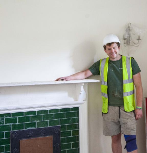 Person wearing a hard hat by a fireplace