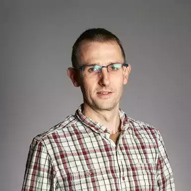 Tom Monie headshot wearing checked shirt and glasses