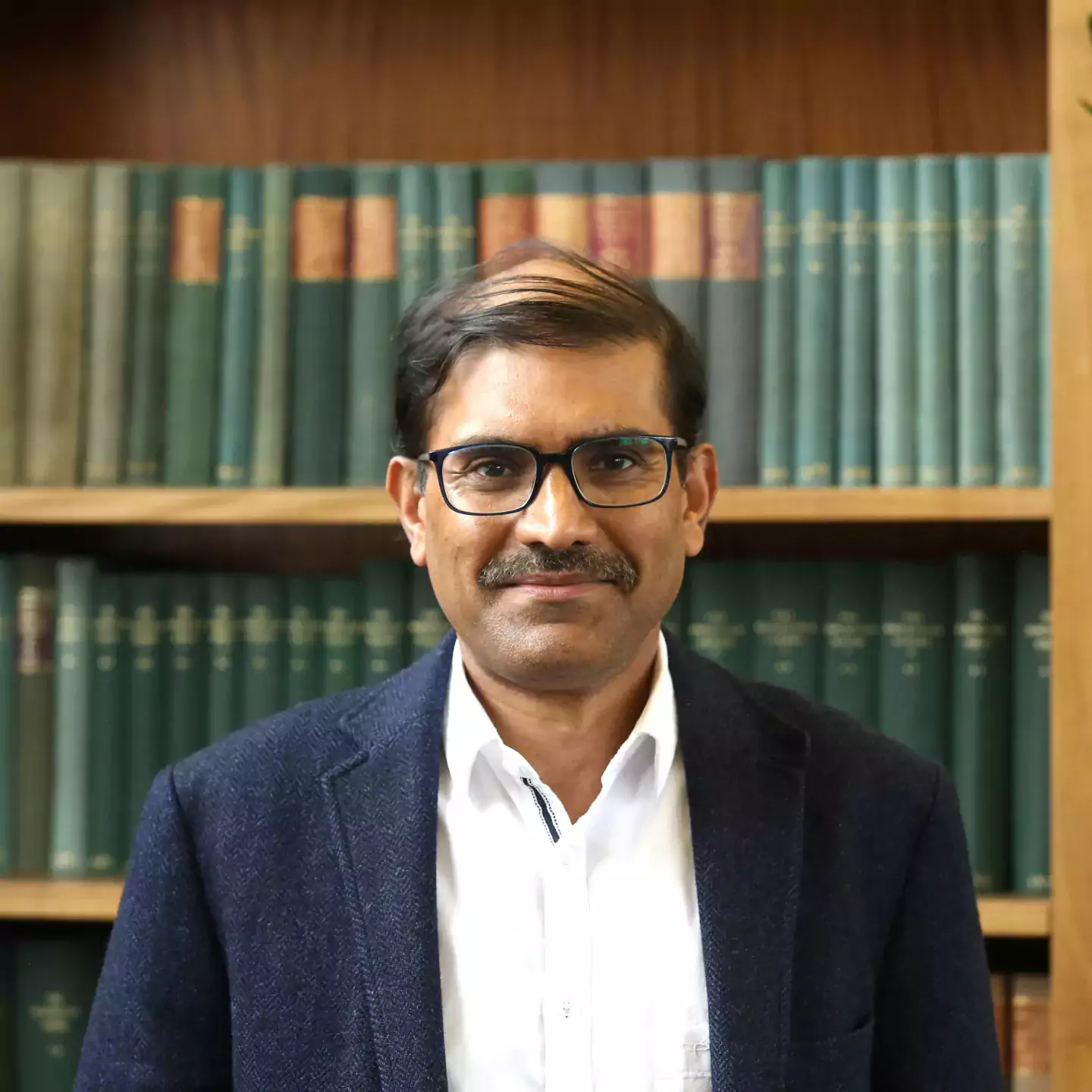 Sanjeev Goyal headshot in front of bookshelves
