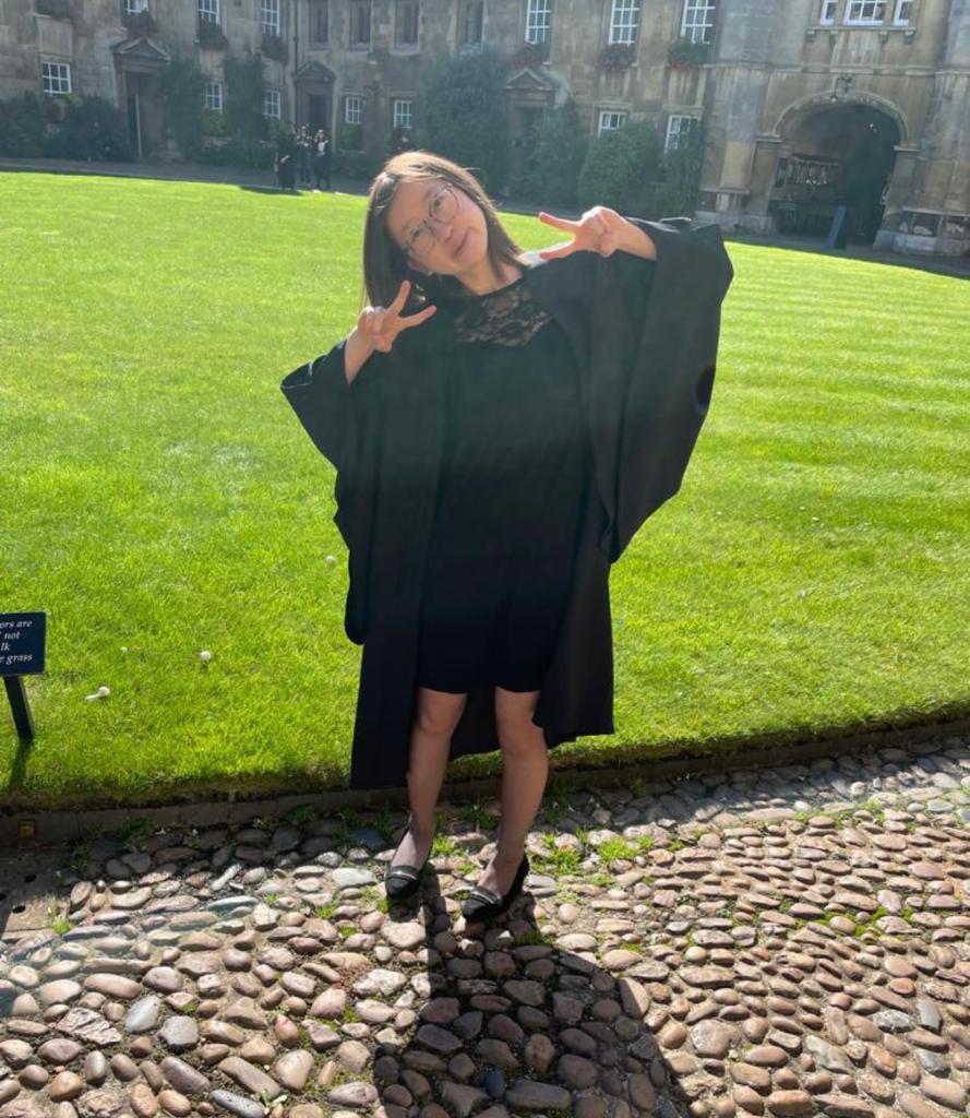 A student in a gown making 'peace' signs, in front of a lawn